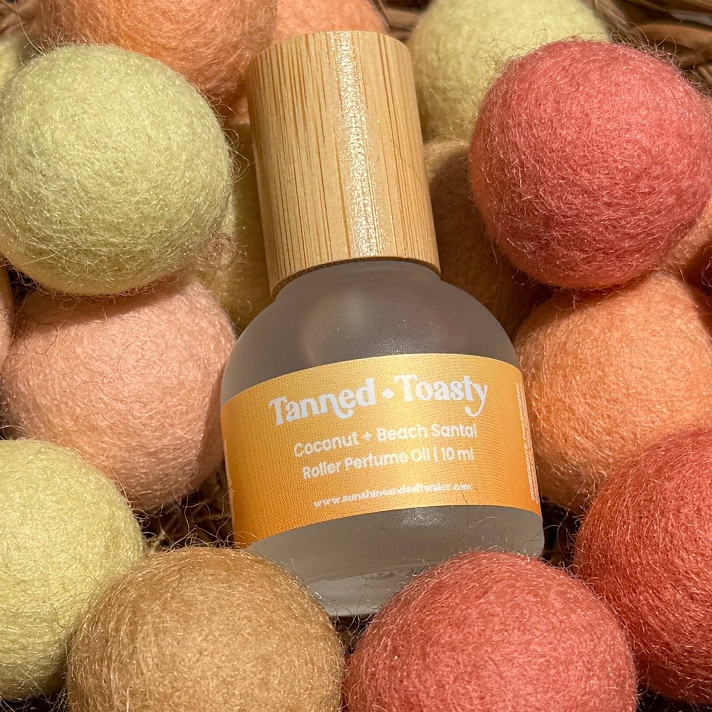 Basket filled with colorful felt balls and a bottle of essential oil on a wooden surface