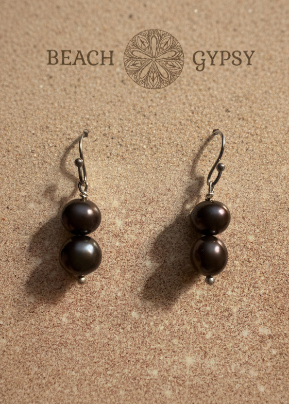 Pair of black pearl earrings on a textured surface with 'Gypsy Beach' branding.
