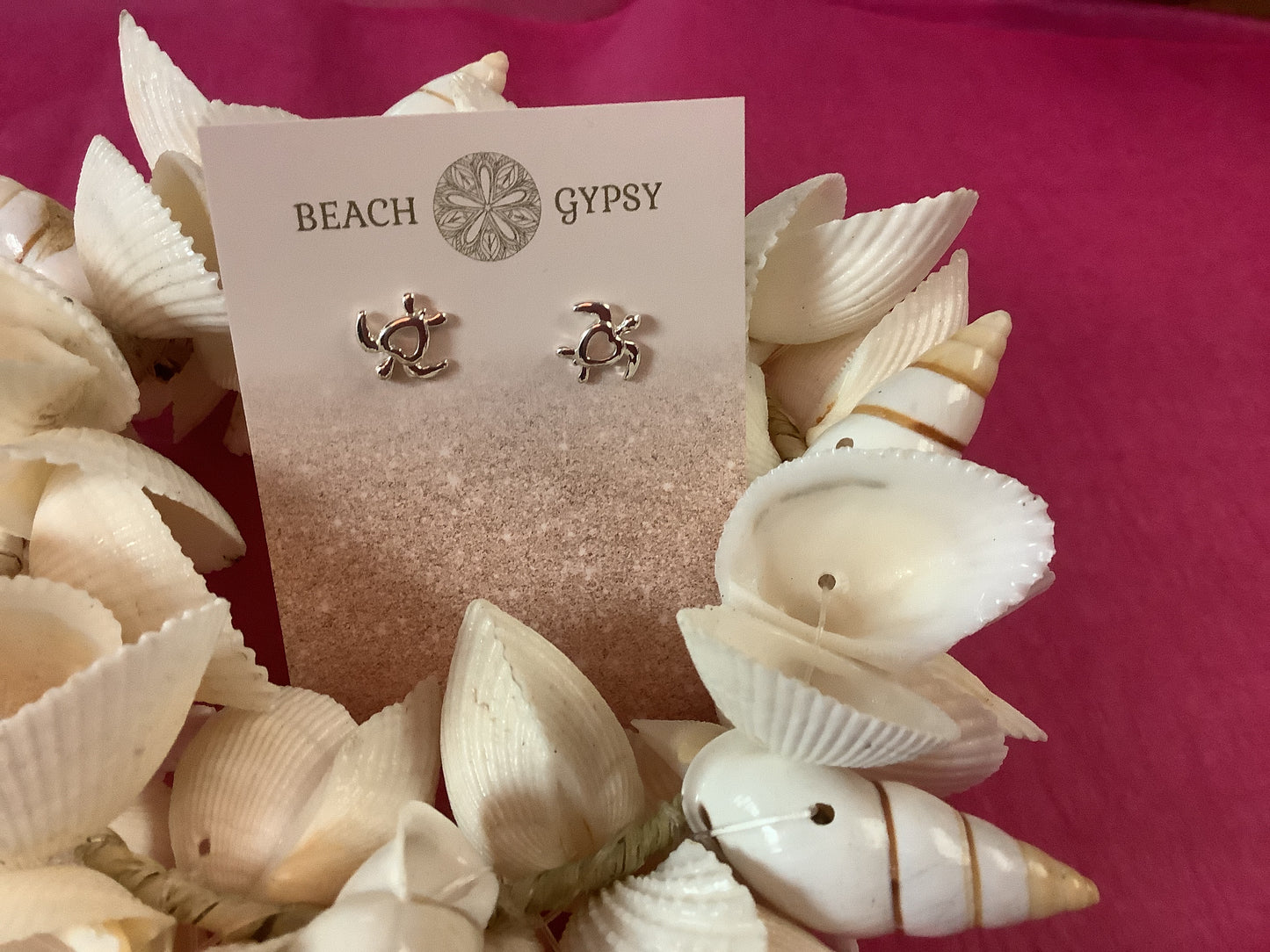 Pair of earrings on a 'Beach Gypsy' card surrounded by seashells on a pink background
