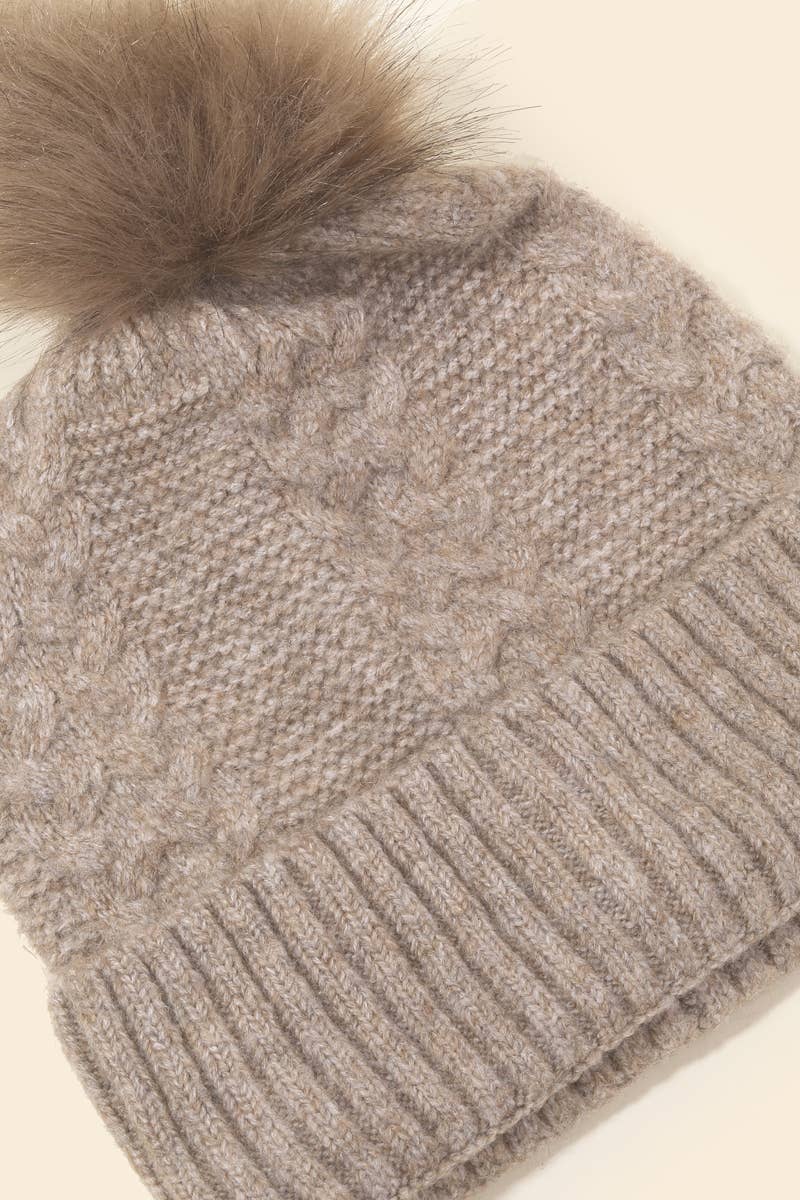 Knitted beanie with a fur pom-pom on a beige background