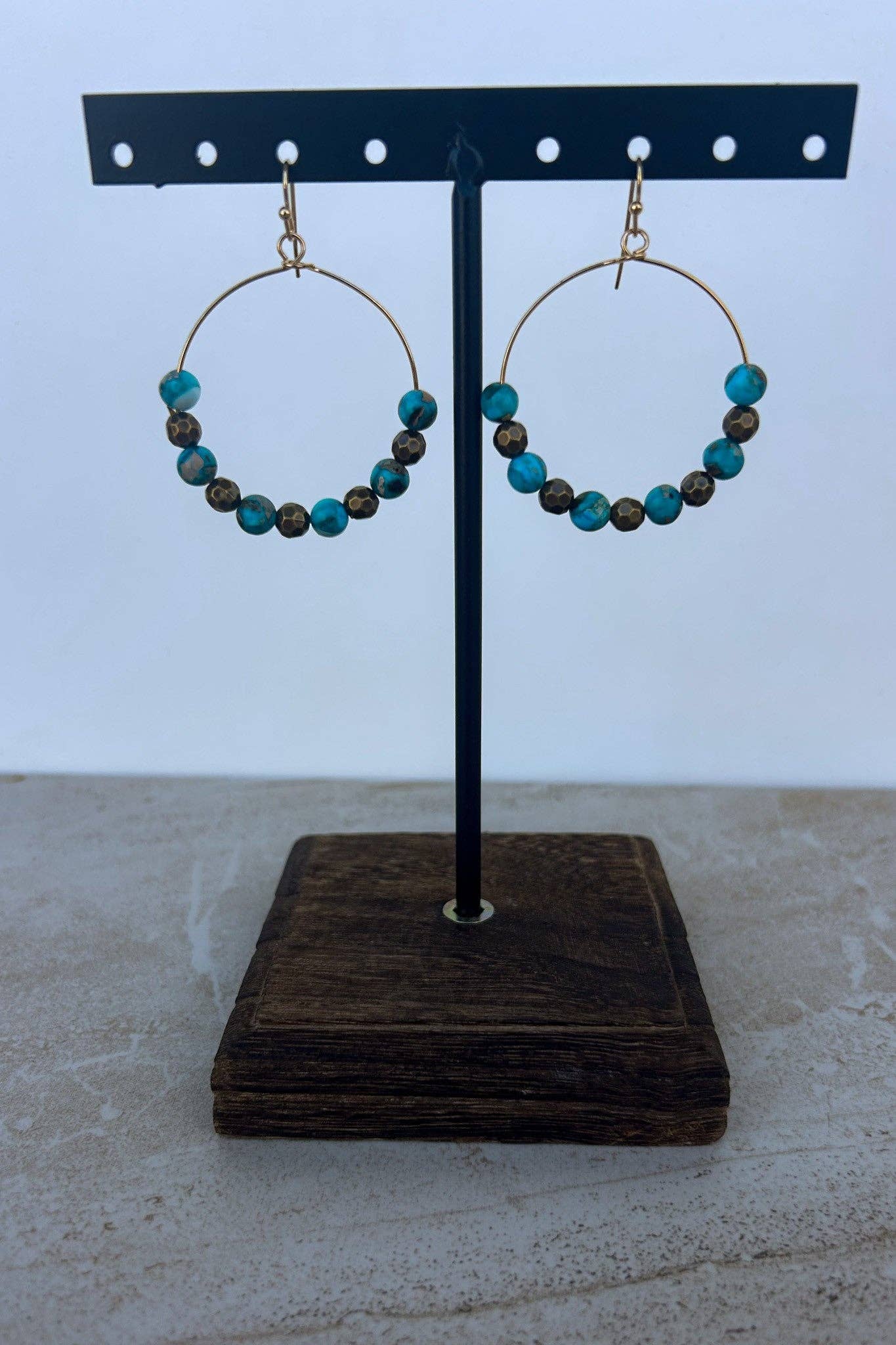Hoop earrings with blue and brown beads on a black stand against a white background