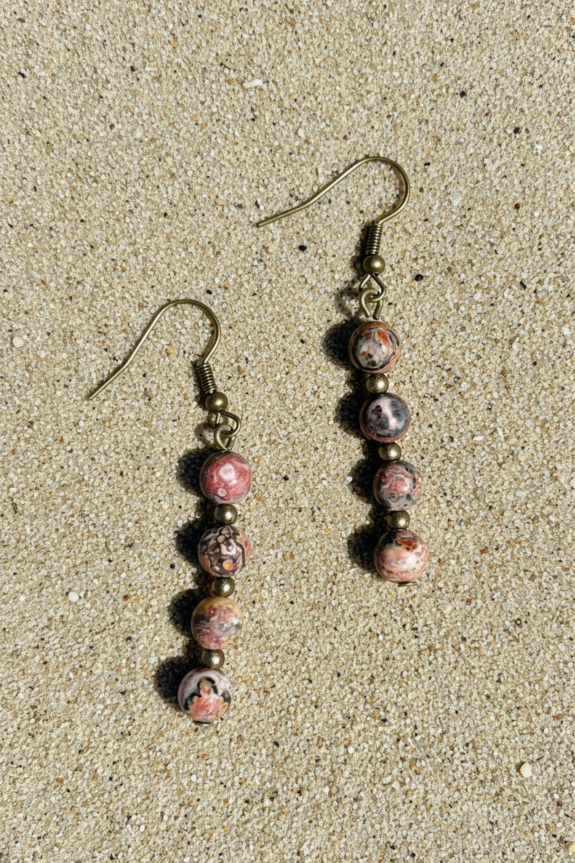 Pair of earrings with pink and brown beads on a sandy surface