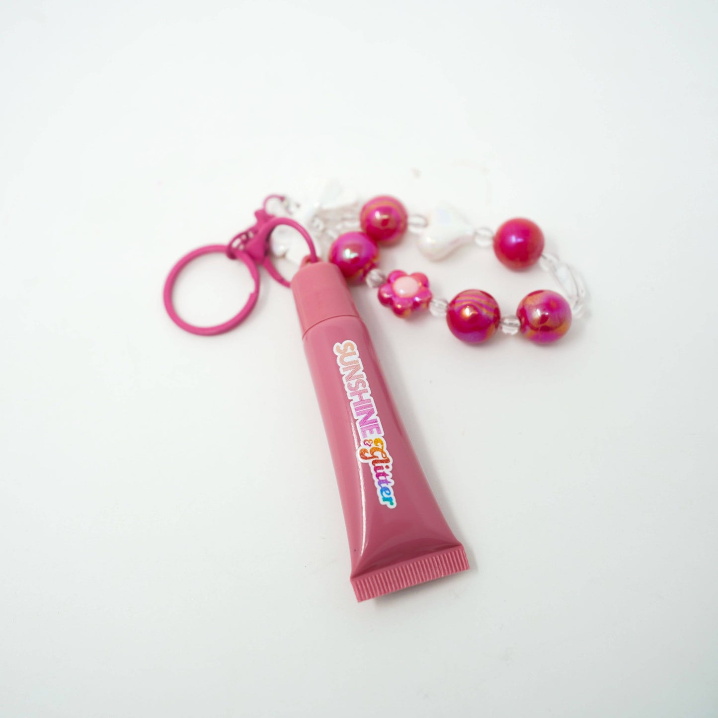 Pink lip gloss with a keychain and beads on a white background