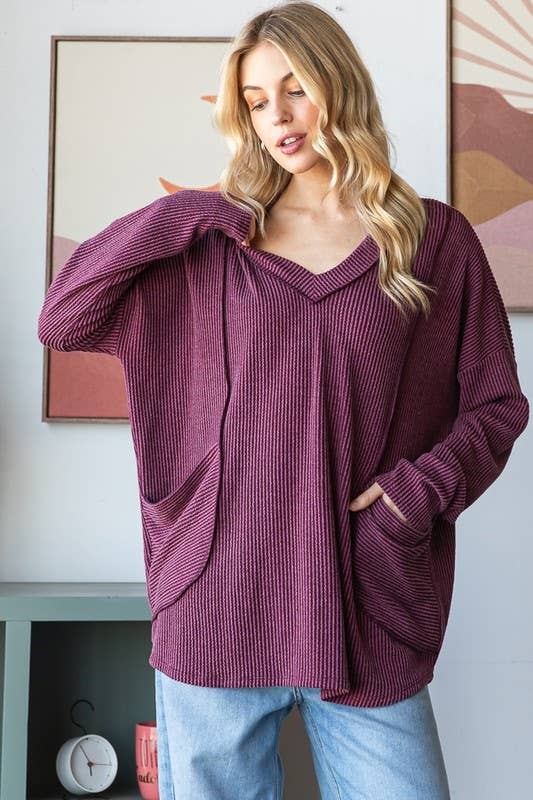 Woman wearing a burgundy sweater with a V-neck and long sleeves, standing indoors.