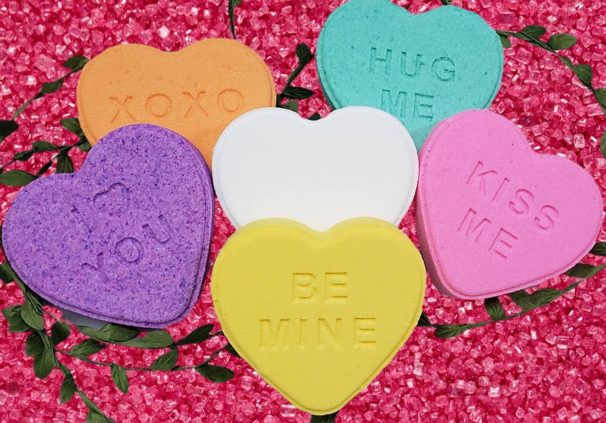 Colorful heart-shaped conversation candies on a pink glittery background
