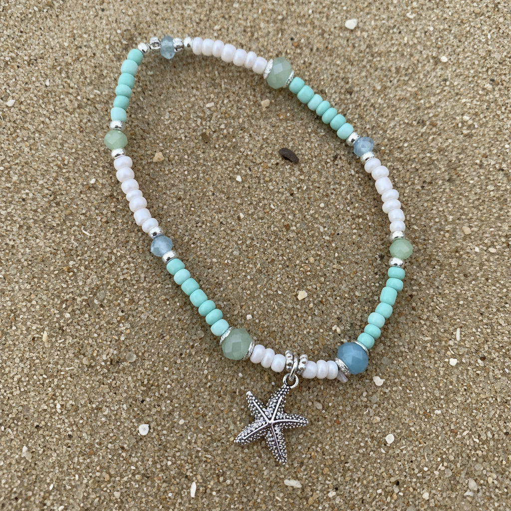 Beaded necklace with a starfish charm on a sand background
