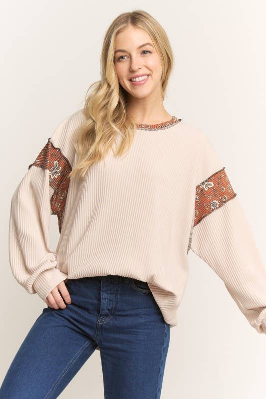 Woman wearing a beige sweater with contrasting fabric on sleeves on a plain background