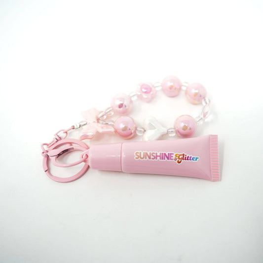 Pink lip balm with 'Sunshine Glitter' text and a beaded keychain on a white background