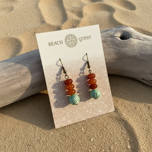 Red agate dangle earrings leaning on driftwood
