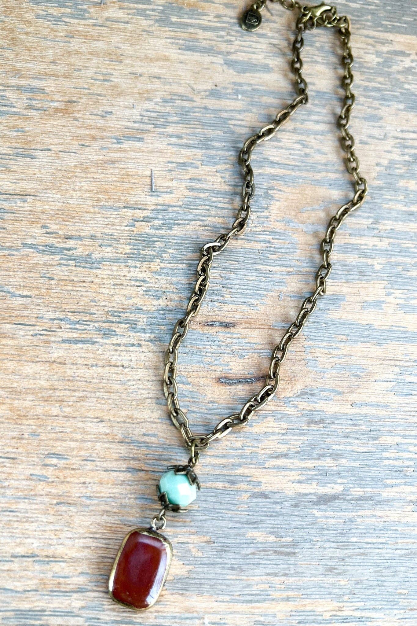 Necklace with a chain, red pendant, and turquoise stone on a wooden surface