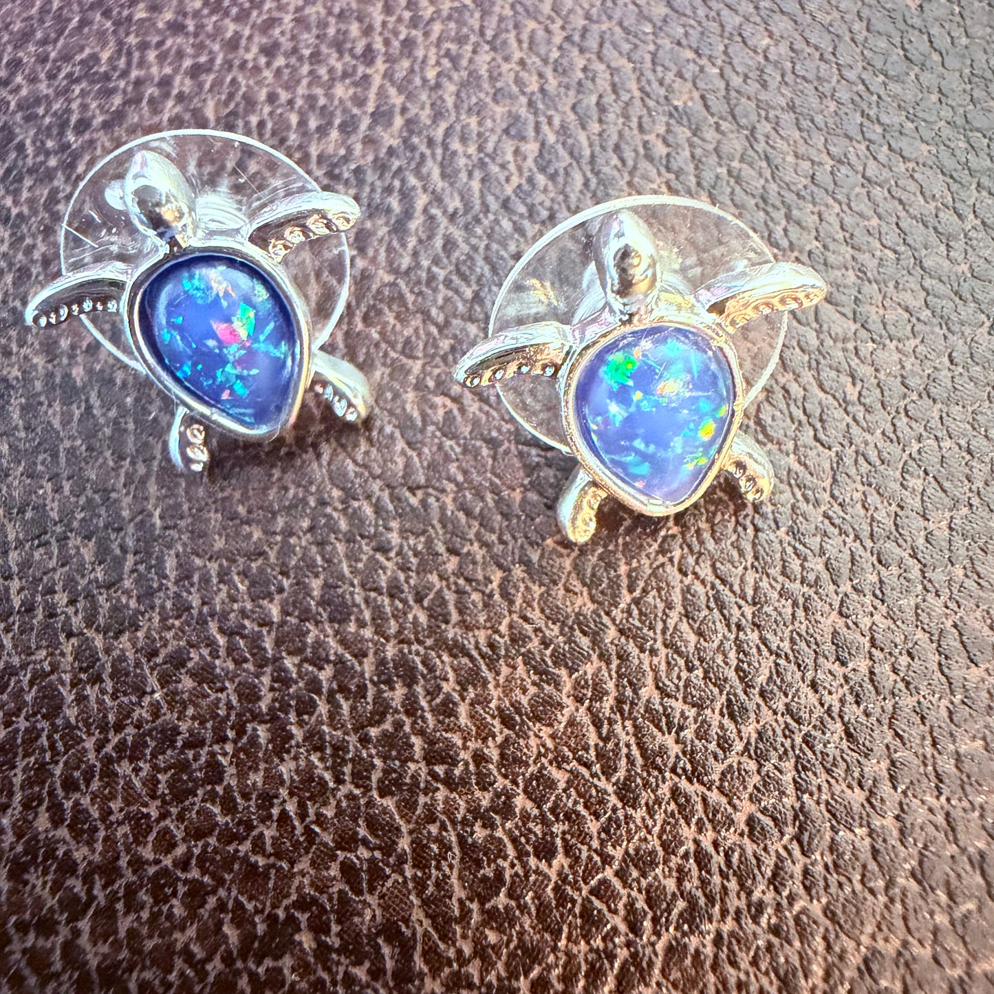 Turtle-shaped earrings with blue gemstones on a textured brown surface