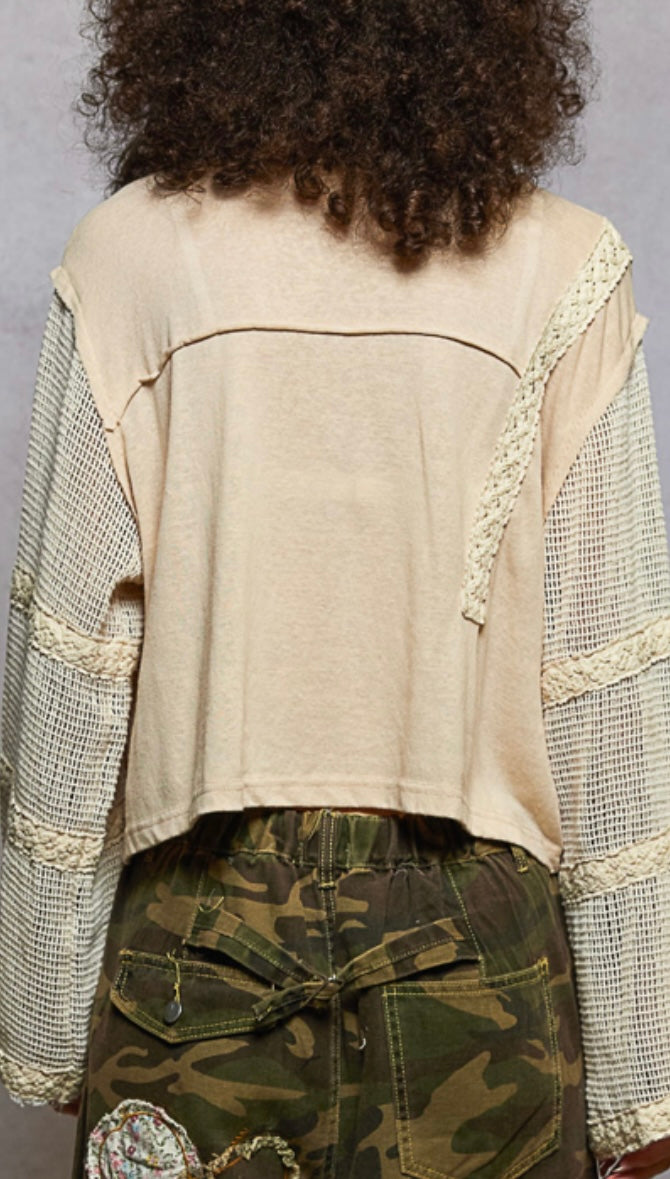 Person wearing a beige top with lace details and camouflage pants against a gray background