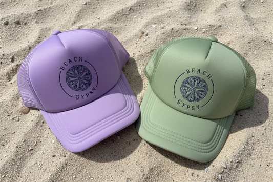 Green and Purple Beach Gypsy trucker hat sitting on a sandy beach surface