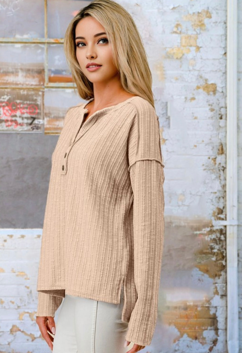 Woman wearing a beige ribbed blouse against a textured wall.