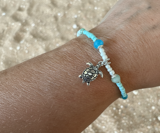 Bracelet with a turtle charm on a wrist against a sandy background