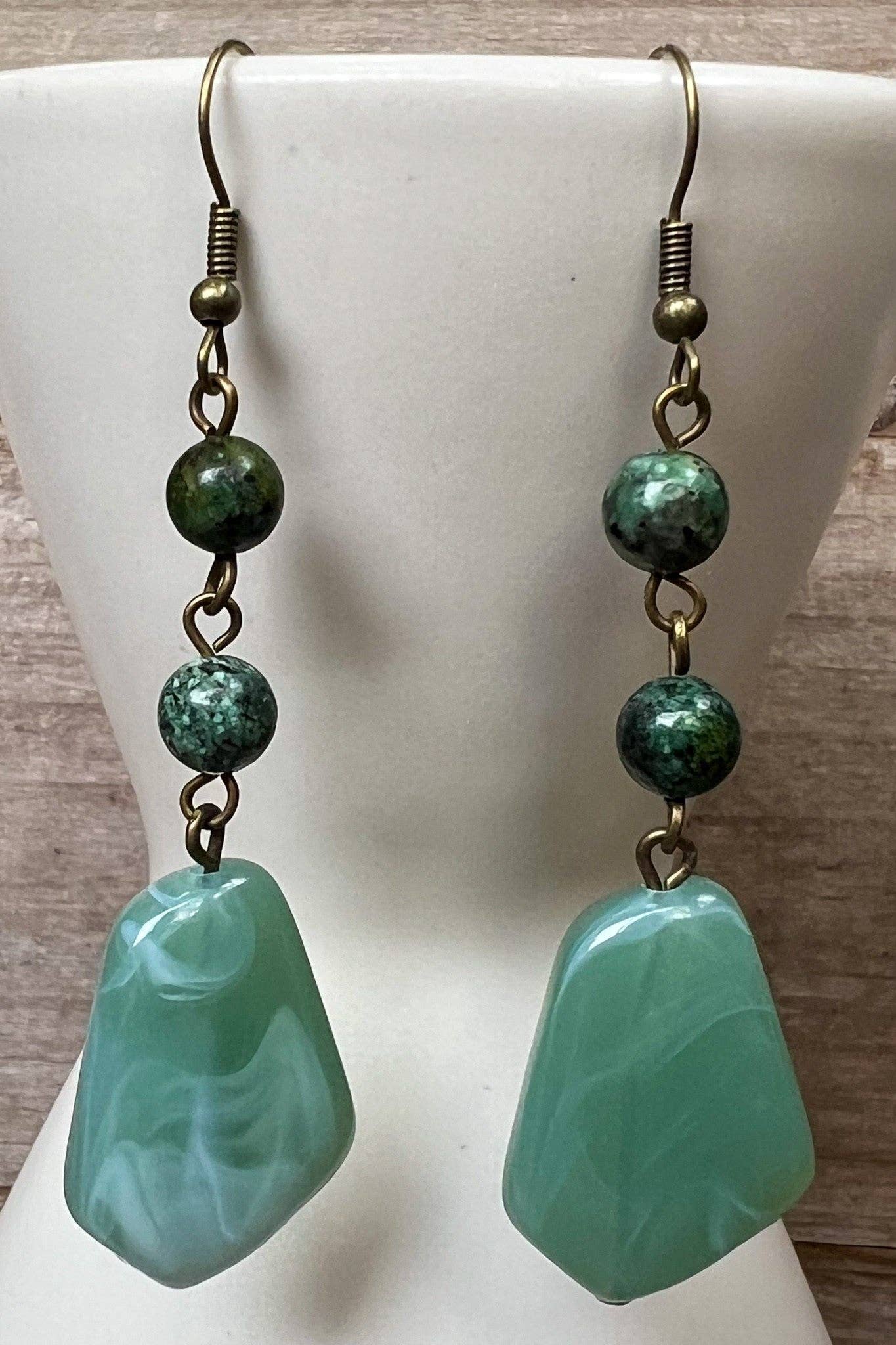 Green stone earrings on a white mannequin bust with a wooden background