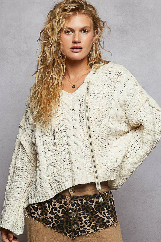 Woman wearing a cream knitted sweater over a white shirt with leopard print shorts on a gray background
