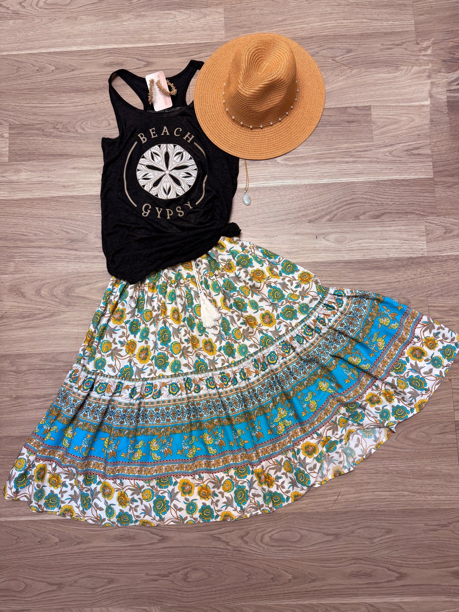 Black Beach GYpsy logo tank top laying on floor with a colorful skirt and a wide brimmed hat and a necklace