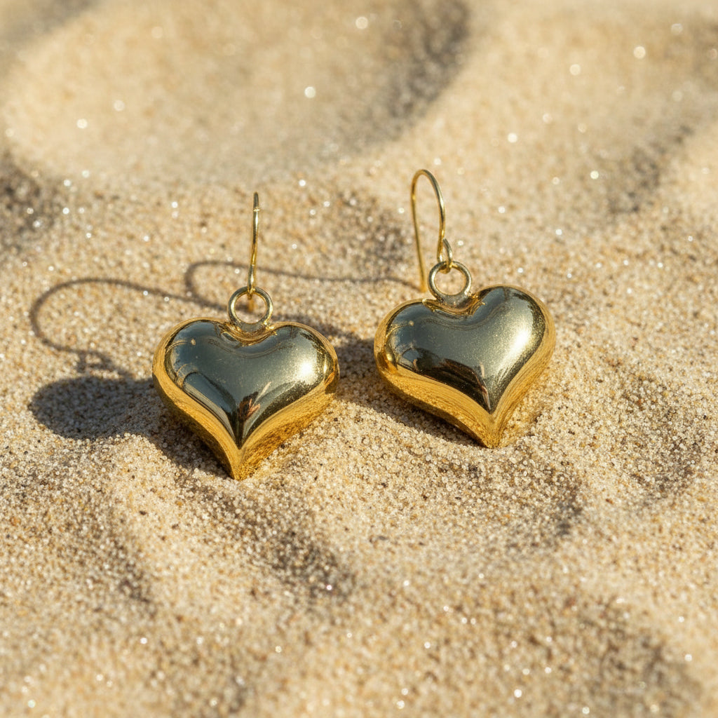 Gold heart-shaped earrings on a sandy background