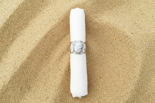 A silver ring with a large oval cabochon stone featuring a black and white marbled pattern, displayed on a white fabric ring holder against a sand background .