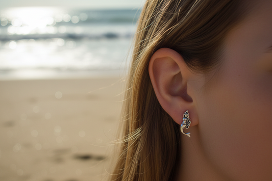 Close-up of an ear with a silver mermaid earring against a beach background
