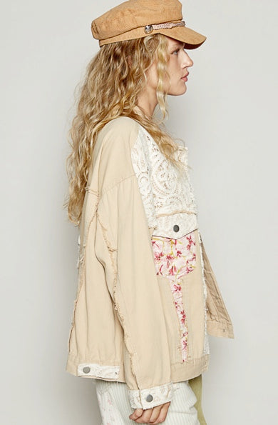Woman wearing a beige jacket with floral embroidery and a matching cap against a plain background