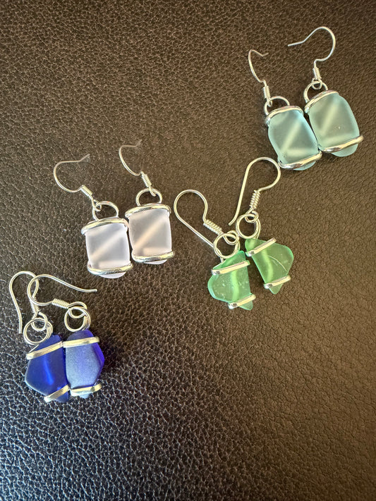 Sets of blue, green, light blue and pink and silver sea glass earrings on a dark textured surface