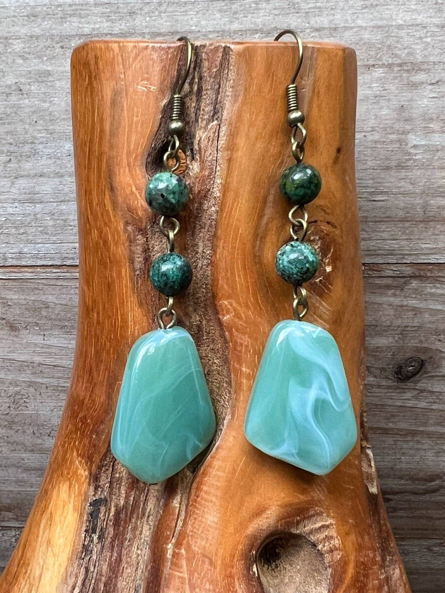 Green stone earrings on a wooden stand with a wooden background