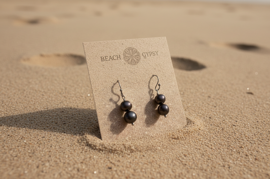 Black pearl earrings on a Beach Gypsy card in the sand. 