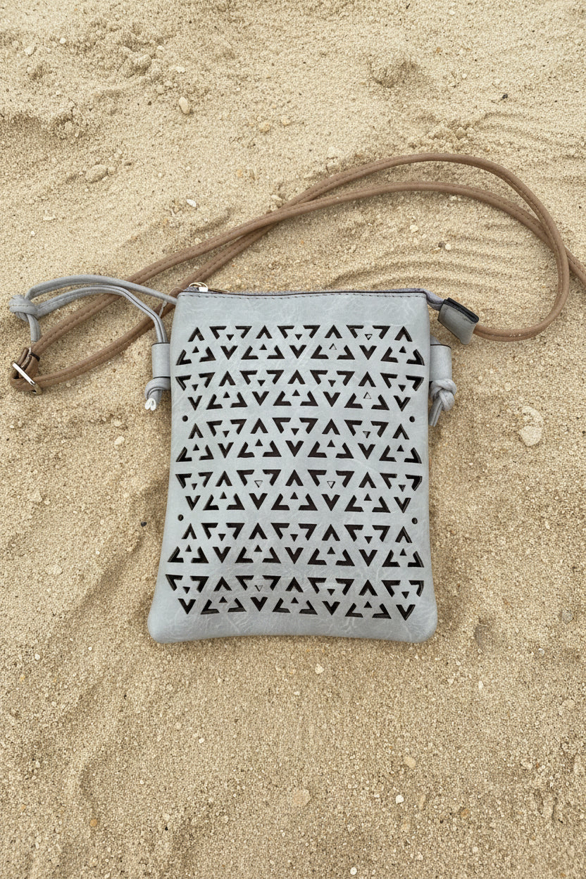 A light gray faux-leather shoulder bag with a geometric triangle cutout pattern, displayed on a bright pink background.