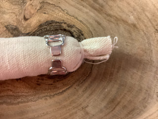A close-up of a silver-toned metal ring with a textured, woven fabric band wrapped around it, resting on a rustic wood slice background.