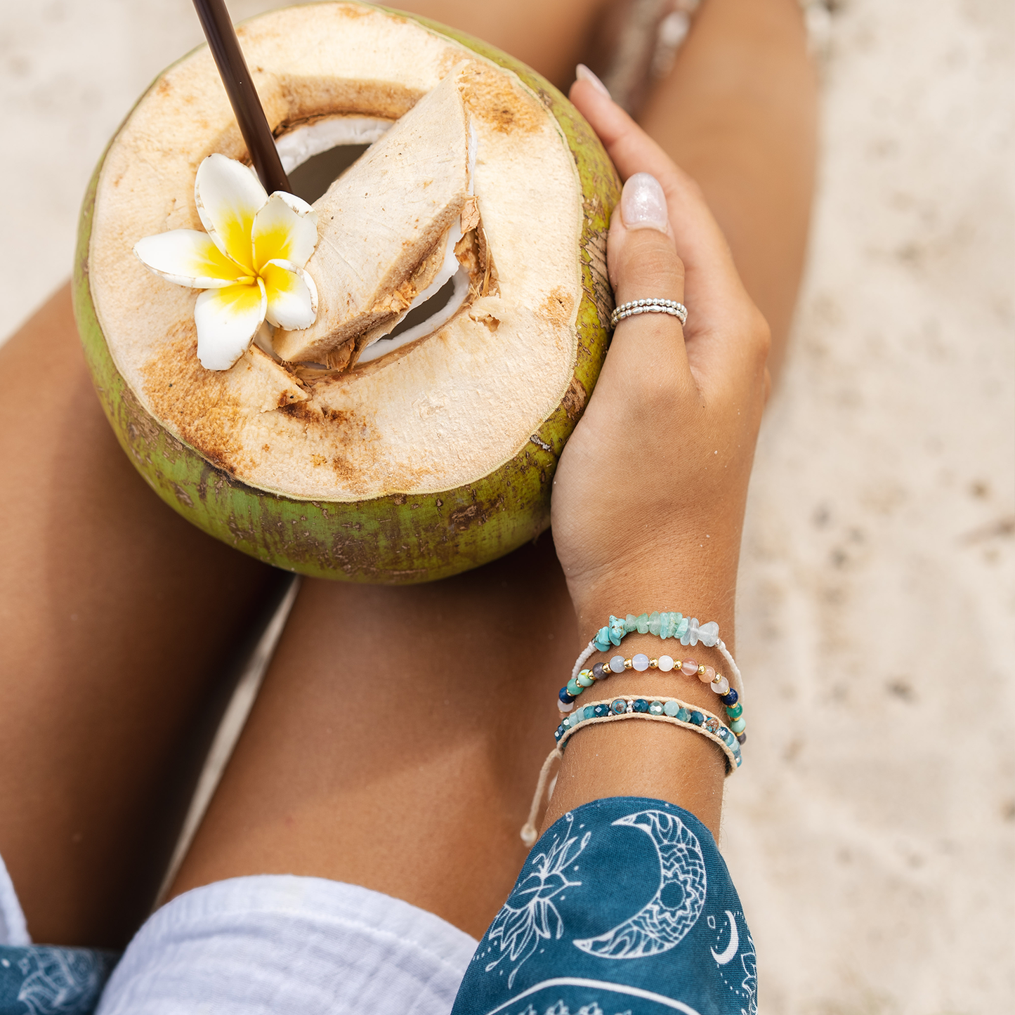 Person holding a fresh coconut with a flower on a beach.