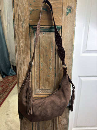Brown Half Moon Fringe Bag with fringe tassels and studded shoulder strap, hanging on a rustic wood door – Beach Gypsy