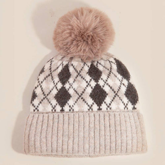 Knitted beanie with argyle pattern and fluffy pom-pom on a beige background