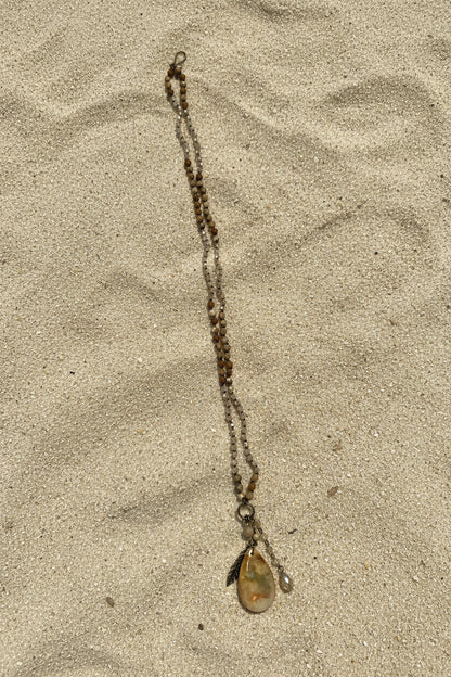 A beaded necklace with a polished oval pendant with a sand background.