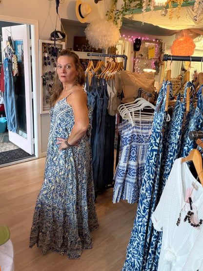 Side view of Contessa Open Back Maxi Dress in a clothing store with racks of clothes.
