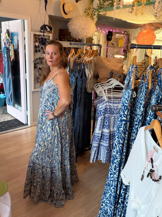 Side view of Contessa Open Back Maxi Dress in a clothing store with racks of clothes.