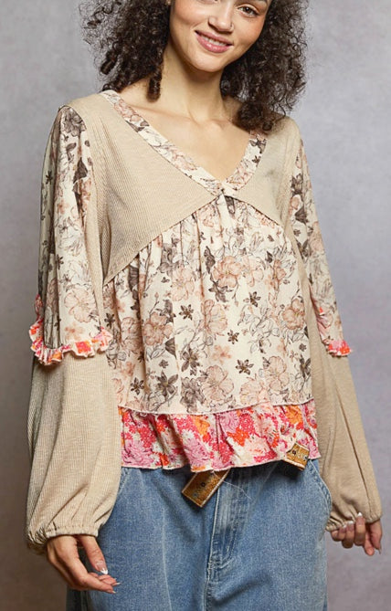 Woman wearing a floral blouse with a beige cardigan and blue jeans against a gray background
