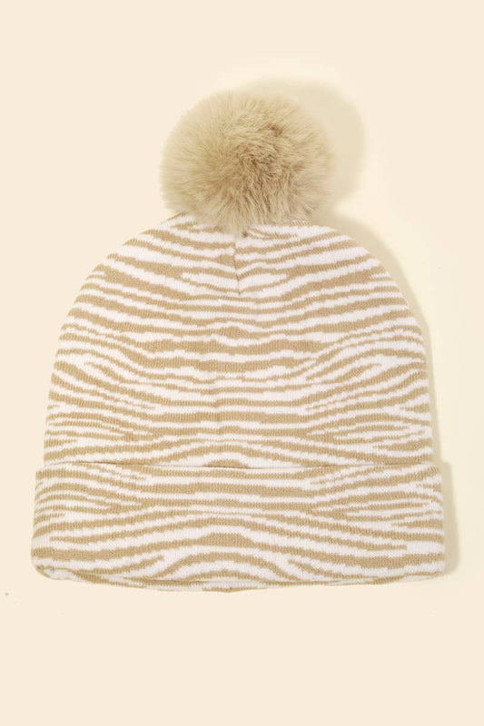 Knitted beanie with zebra pattern and fur pom-pom on a beige background