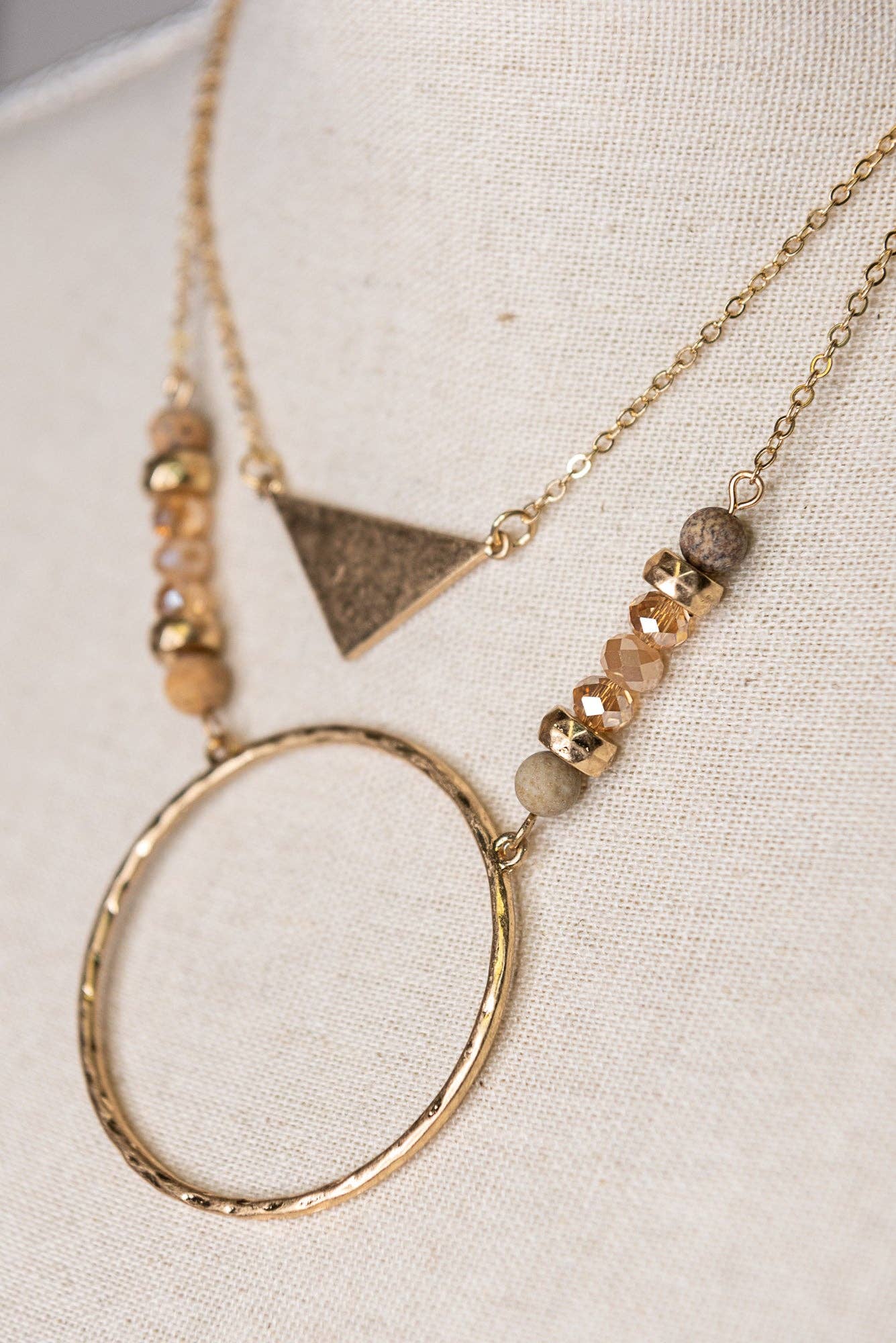 Necklace with geometric pendant and beaded chain on a textured surface