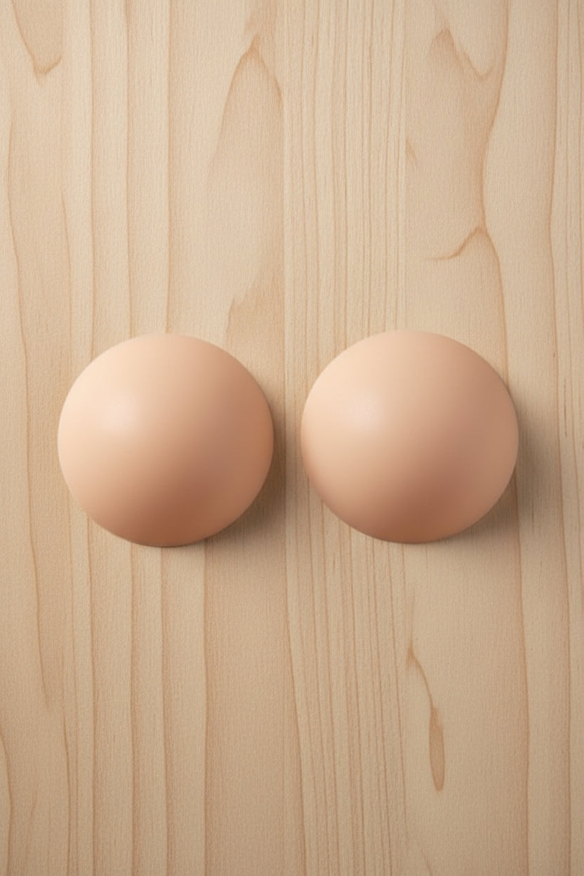Pair of nude-colored circular pasties on a light colored wooden surface
