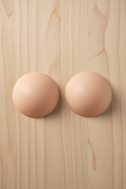 Pair of nude-colored circular pasties on a light colored wooden surface