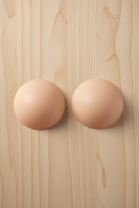 Pair of nude-colored circular pasties on a light colored wooden surface