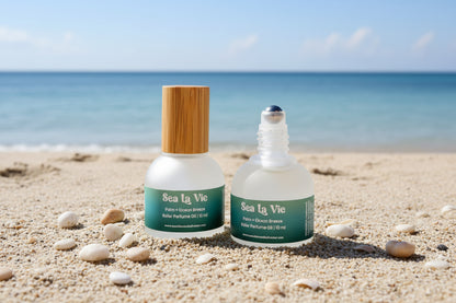 Two bottles of Sea La Vie perfume oil with different bottle designs on a beach background