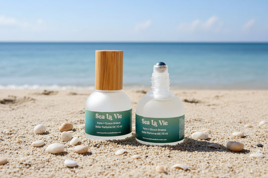 Two bottles of Sea La Vie perfume oil with different bottle designs on a beach background