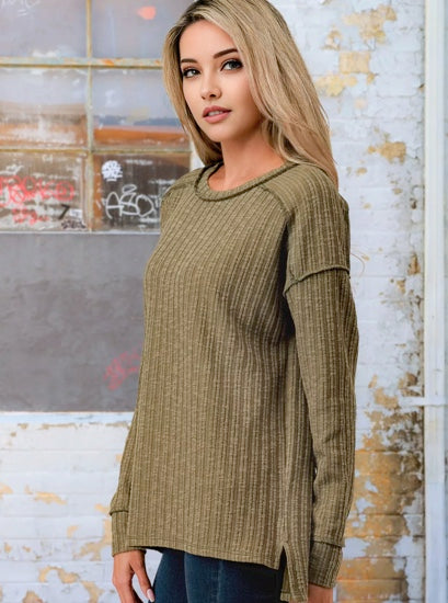 Woman wearing a green ribbed sweater in front of a textured wall.