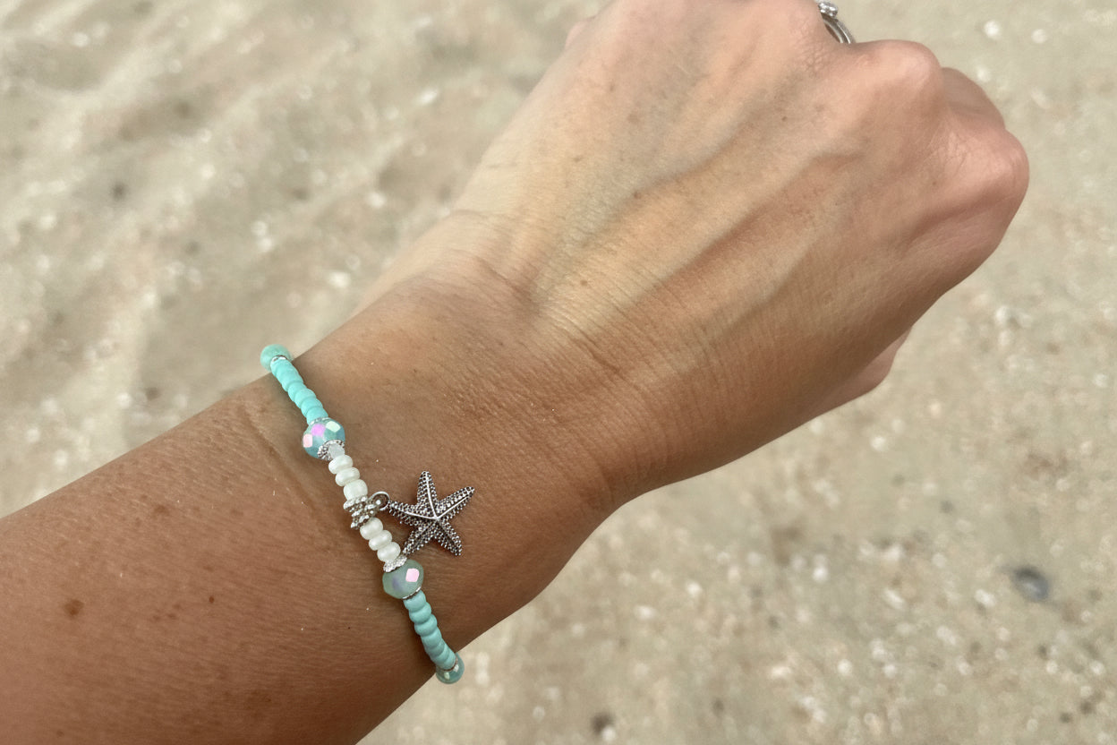 Hand wearing a bracelet with a starfish charm on a beach background