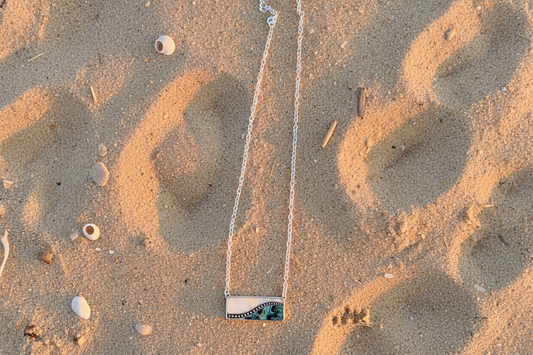 Mother of pearl and abalone rectangular pendant on a silver c9lored necklace on a beach