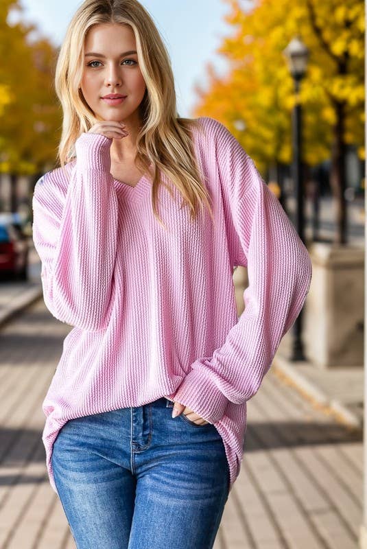 Woman wearing a pink sweater and blue jeans standing outdoors with trees in the background.