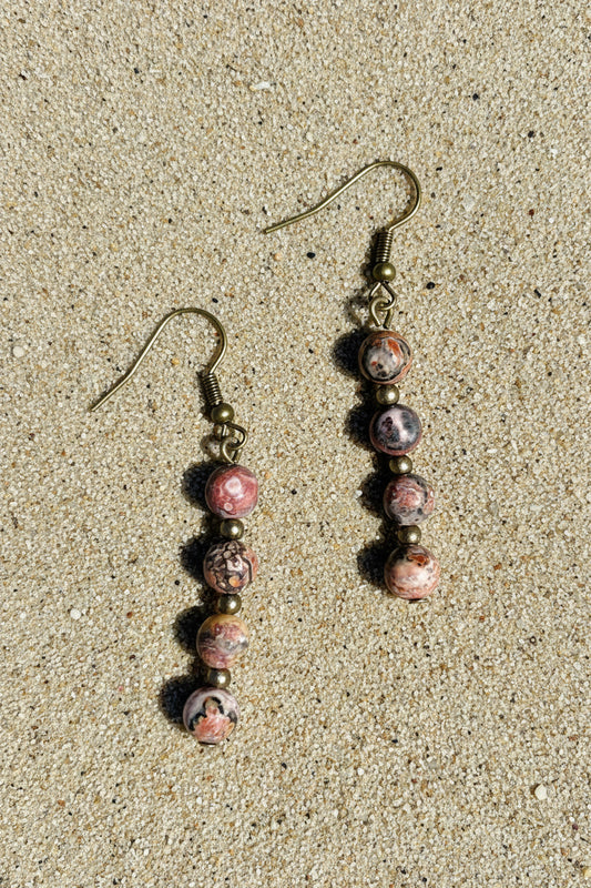 Pair of earrings with pink and brown beads on a sandy surface